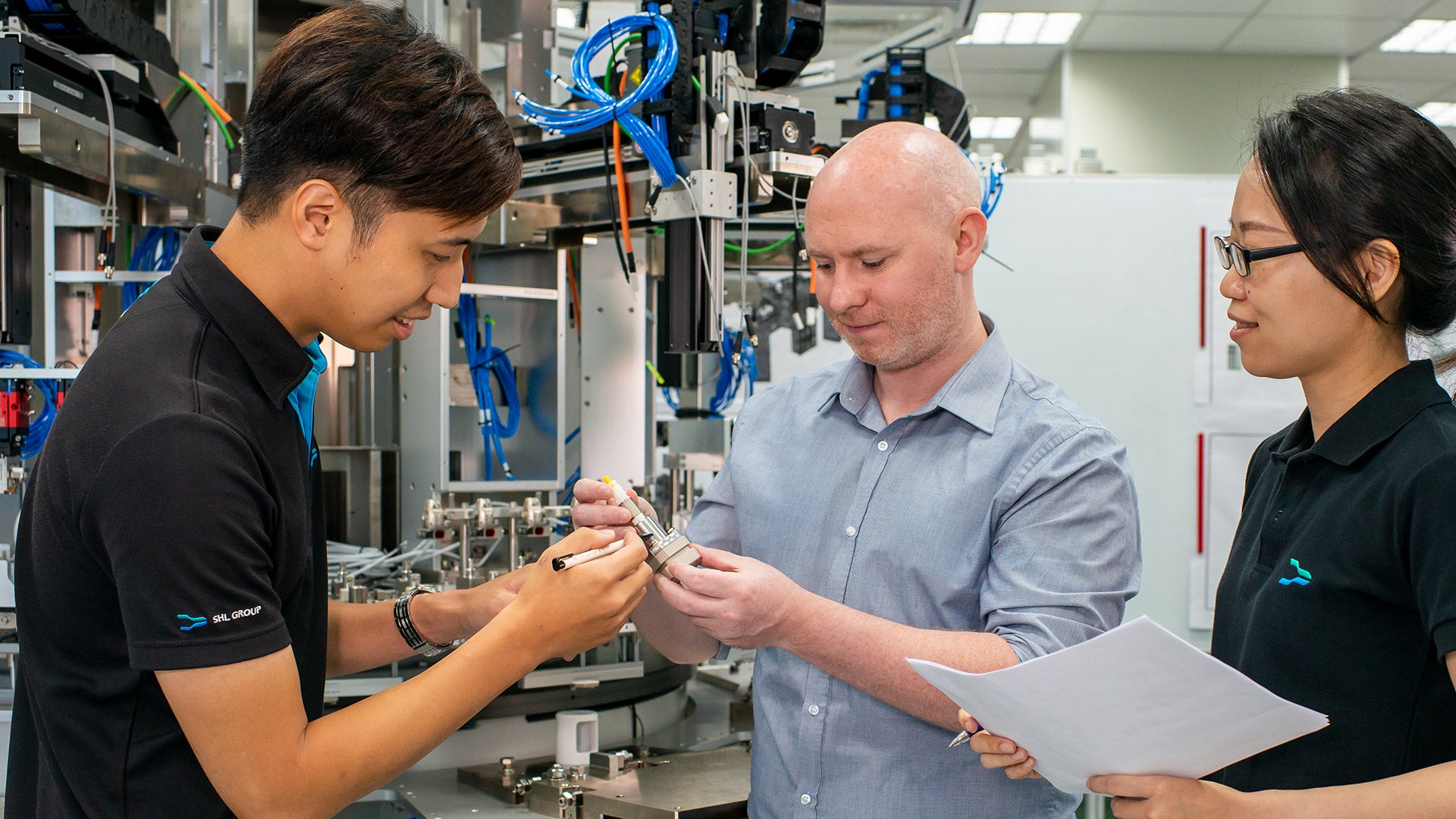 Project engineers inspecting an autoinjector component in front of a fully